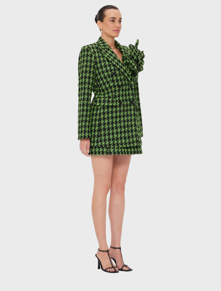 A woman wearing a green and black checkered blazer dress, standing confidently with a neutral background.