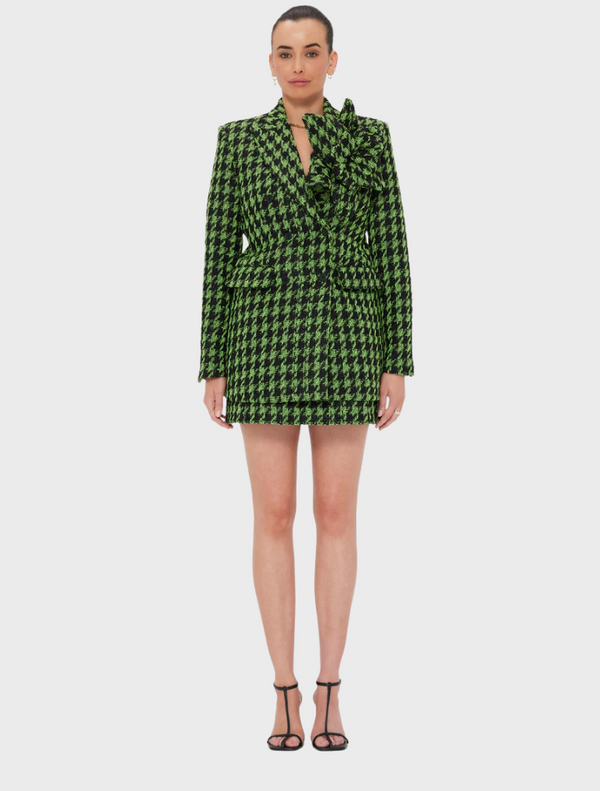 A woman wearing a green and black checkered blazer dress, standing confidently with a neutral background.