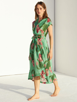 Green linen dress hanging on a wooden hanger against a neutral background, showcasing its simple and elegant design.