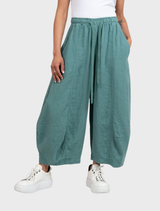 Grass-colored linen trousers displayed on a neutral background, showcasing their lightweight fabric and relaxed fit.