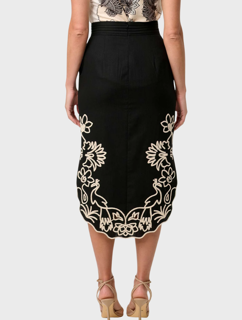 Back view of a woman in a black midi skirt with white embroidery, showcasing the Cascadia Embroidered Linen Viscose design.