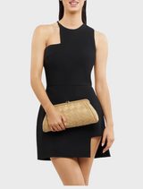 A woman in a black dress holds a natural Lois Woven Frame Bag with a gold clutch, showcasing elegant style.