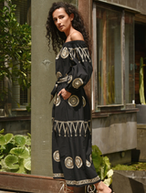 A woman in a fitted black dress leans against a wall, embodying a chic and confident style.