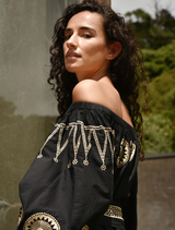 . A woman in a fitted black dress leans against a wall, embodying a chic and confident style.