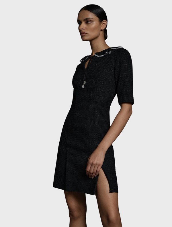 A model poses in a sleek black dress featuring a stylish slit along the side.
