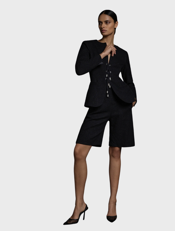 A woman wearing a black suit with shorts, standing confidently with her hands on her hips.