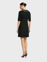 A model wears an elegant black dress with a prominent slit, combining classic and contemporary fashion elements.