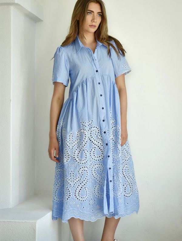  A woman wearing a blue dress adorned with white lace details stands gracefully.