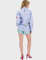 A woman sporting a vivid shirt and shorts stands in a sunny setting, reflecting a playful and energetic fashion choice.