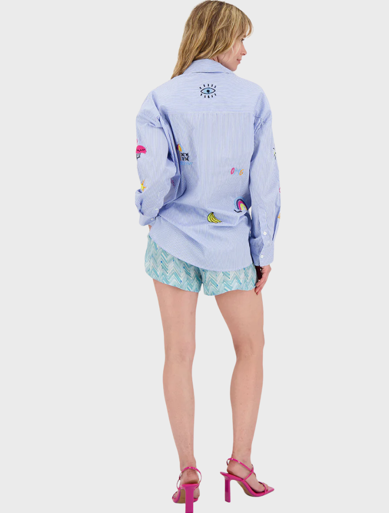A woman sporting a vivid shirt and shorts stands in a sunny setting, reflecting a playful and energetic fashion choice.