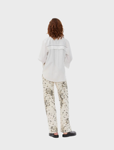 White oversized shirt with broderie anglaise details, long wide sleeves with slits, collar, and front button closure.
