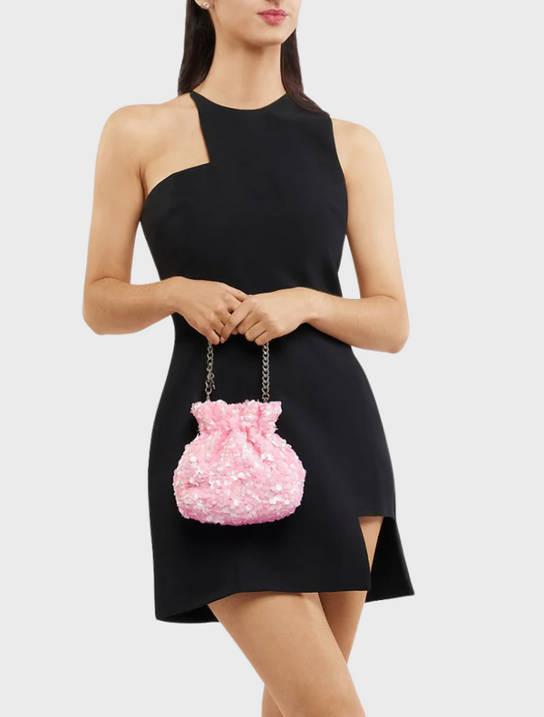 A woman in a black dress holds a pink Mattie Sequin Pouch purse, showcasing a stylish and elegant look.