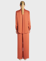 A pair of copper Maxi Pace Pants hanging, highlighting their modern style and smooth material.