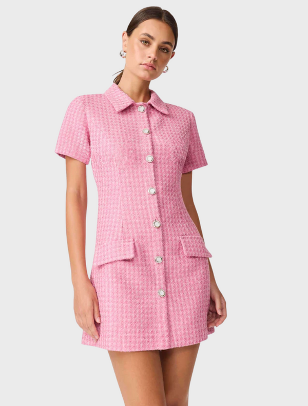 The model is dressed in a pink shirt dress adorned with buttons.