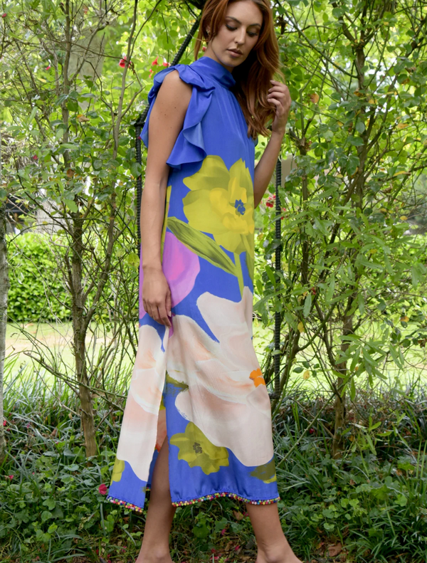 In a garden, a woman wears a cobalt floral dress and pink sandals, exuding elegance and style.