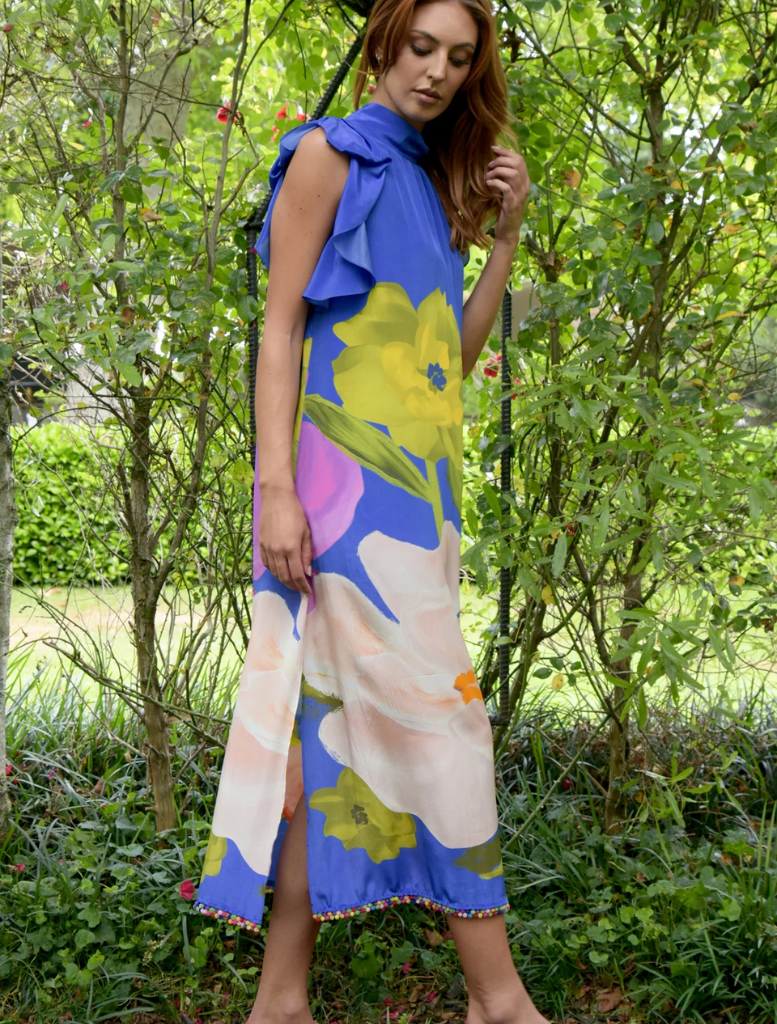In a garden, a woman wears a cobalt floral dress and pink sandals, exuding elegance and style.