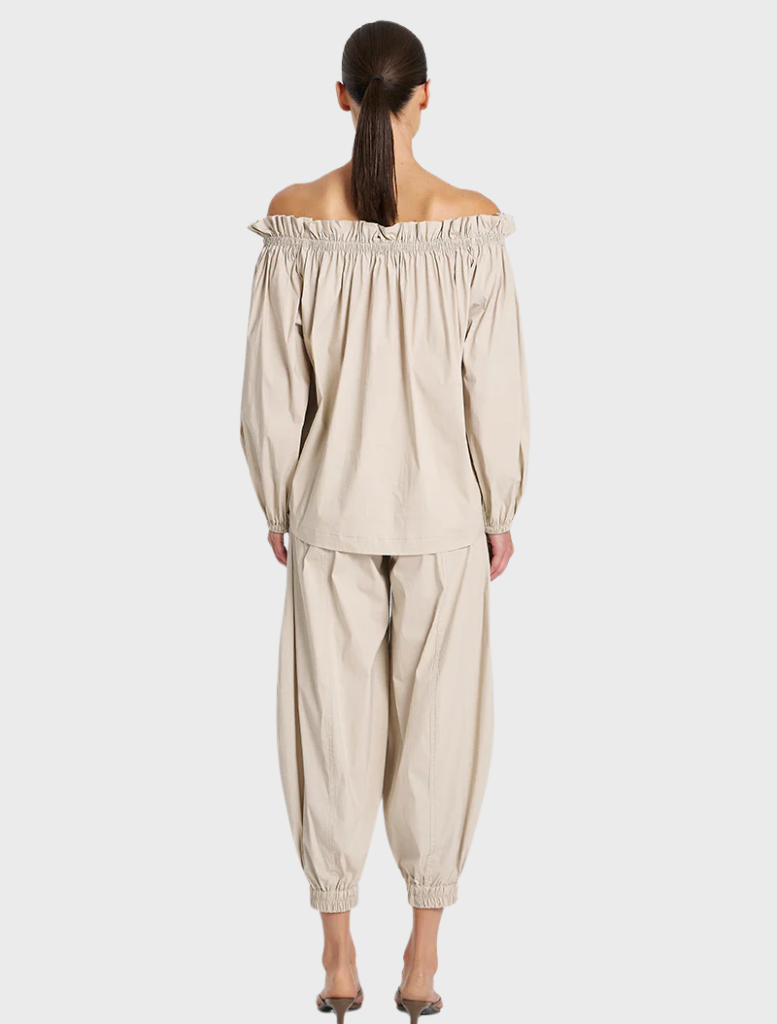 The model displays a stylish off-the-shoulder top and sleek pants, embodying a fashionable and modern aesthetic.
