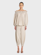 A model poses in an off-the-shoulder top paired with stylish pants, showcasing a chic and modern outfit.