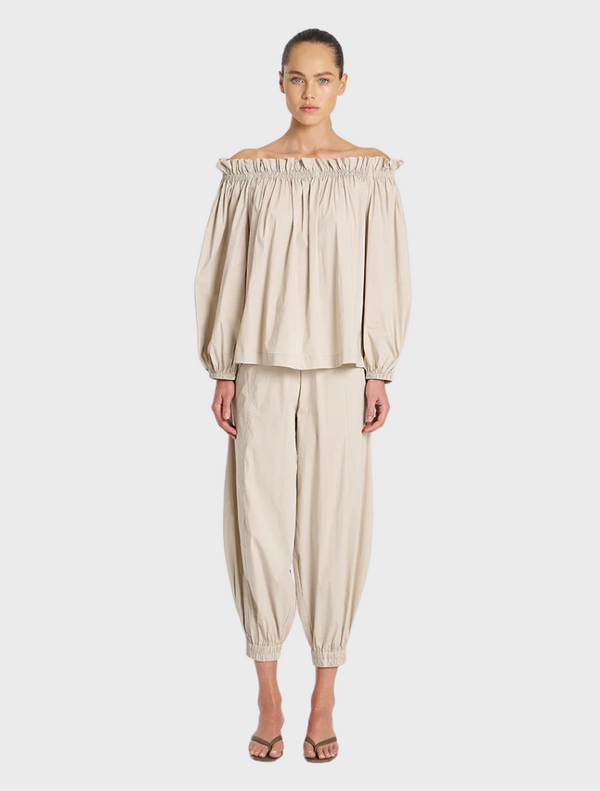 A model poses in an off-the-shoulder top paired with stylish pants, showcasing a chic and modern outfit.