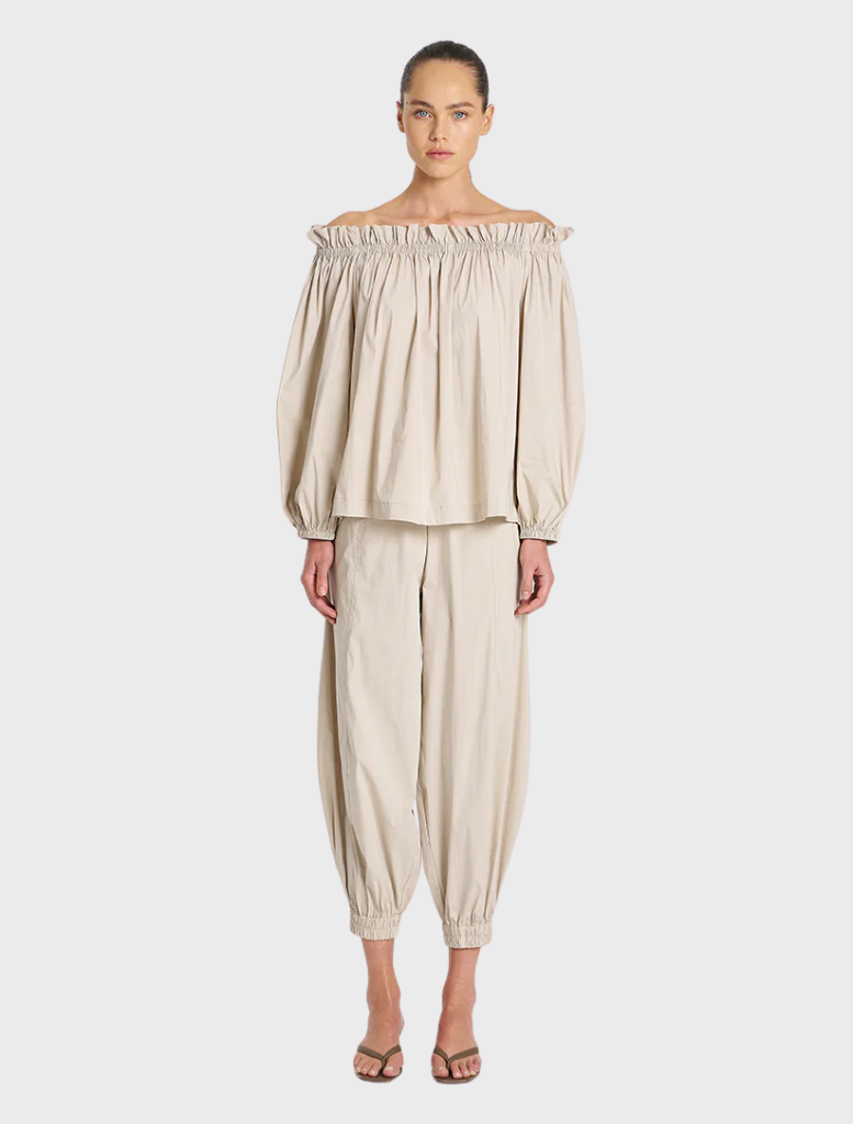 A model poses in an off-the-shoulder top paired with stylish pants, showcasing a chic and modern outfit.