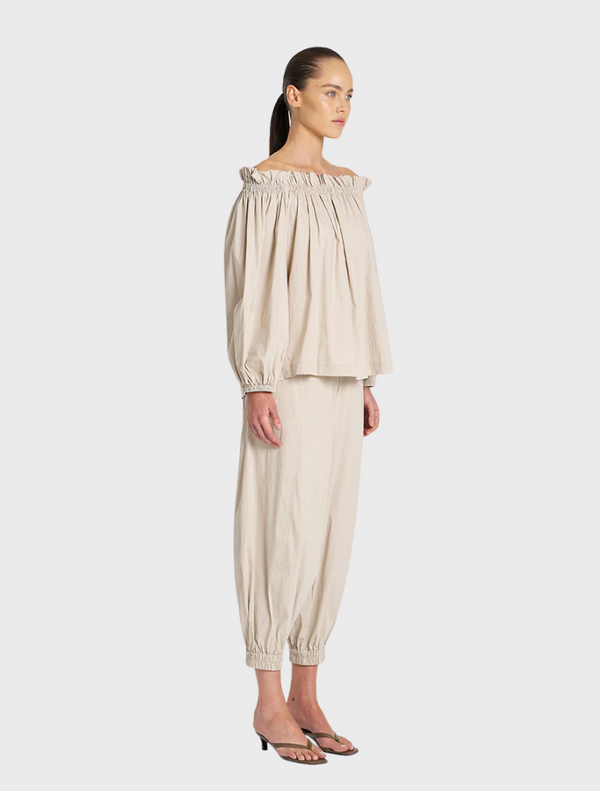 The model showcases a fashionable off-the-shoulder top and tailored pants, highlighting contemporary style.