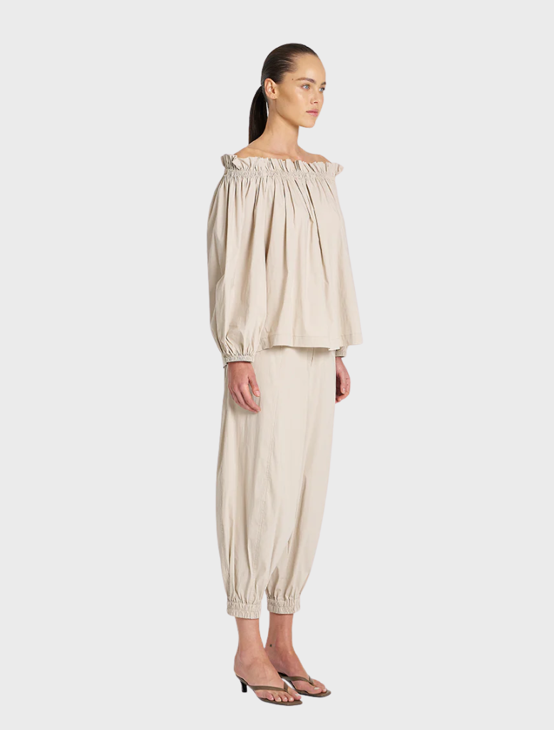 The model showcases a fashionable off-the-shoulder top and tailored pants, highlighting contemporary style.