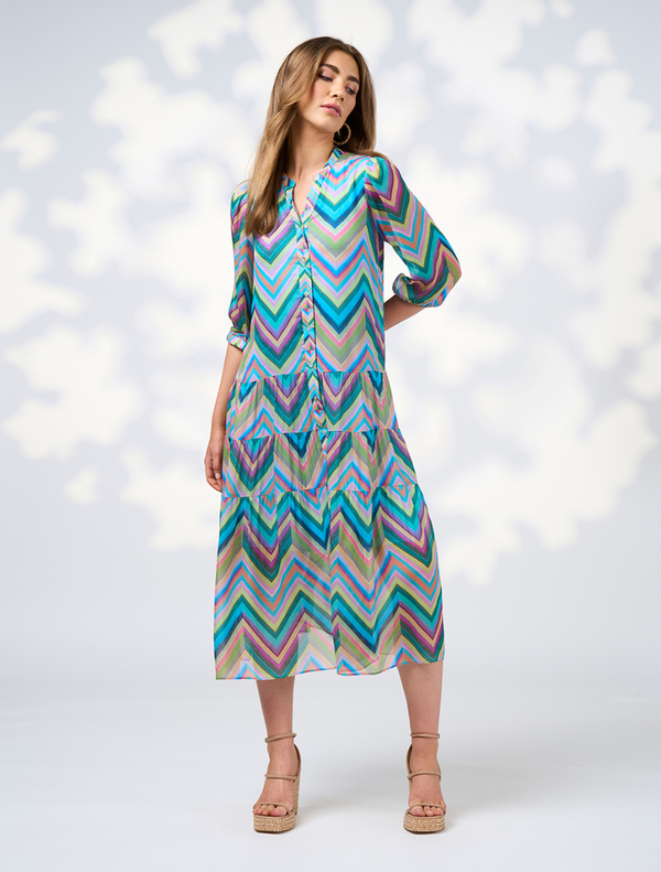 A woman in a blue jacket paired with a vibrant multi-colored Wanderlust Midi Dress.
