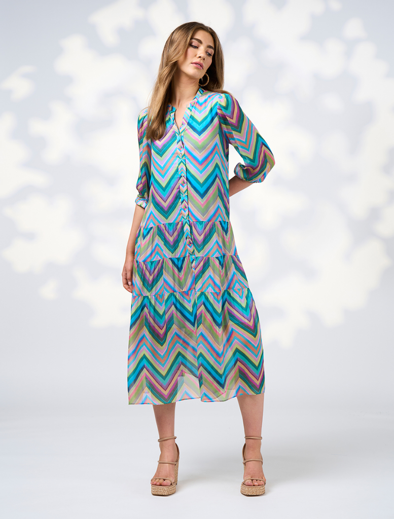 A woman in a blue jacket paired with a vibrant multi-colored Wanderlust Midi Dress.
