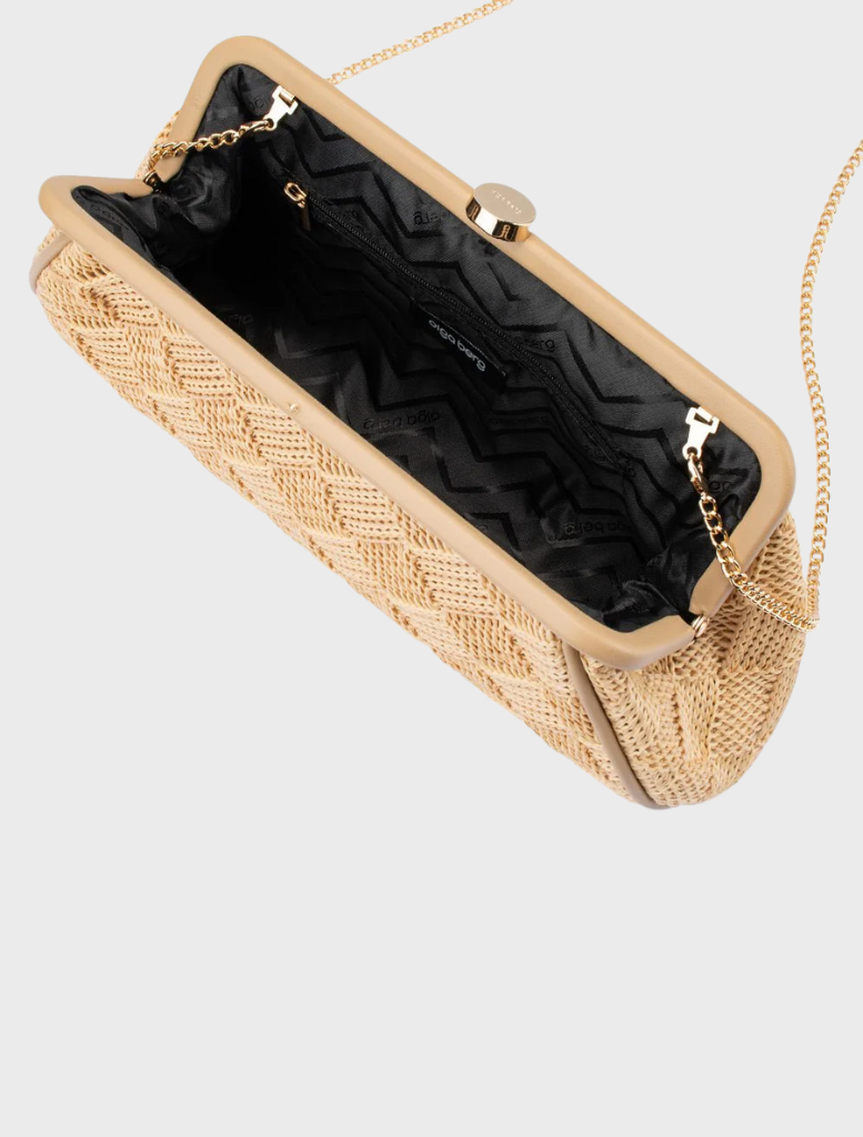 The Lois Woven Frame Bag - Natural a beige woven clutch, is hanging on a hook.