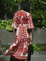 A woman in a vibrant red and white dress stands against a wall, exuding confidence and grace.