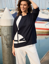 A woman in a navy color block top and white pants poses on a dock, with water visible in the background.