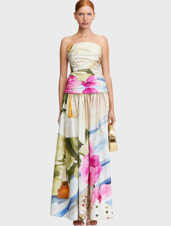 A model showcases a vibrant floral print dress, featuring colorful flowers against a light background.
