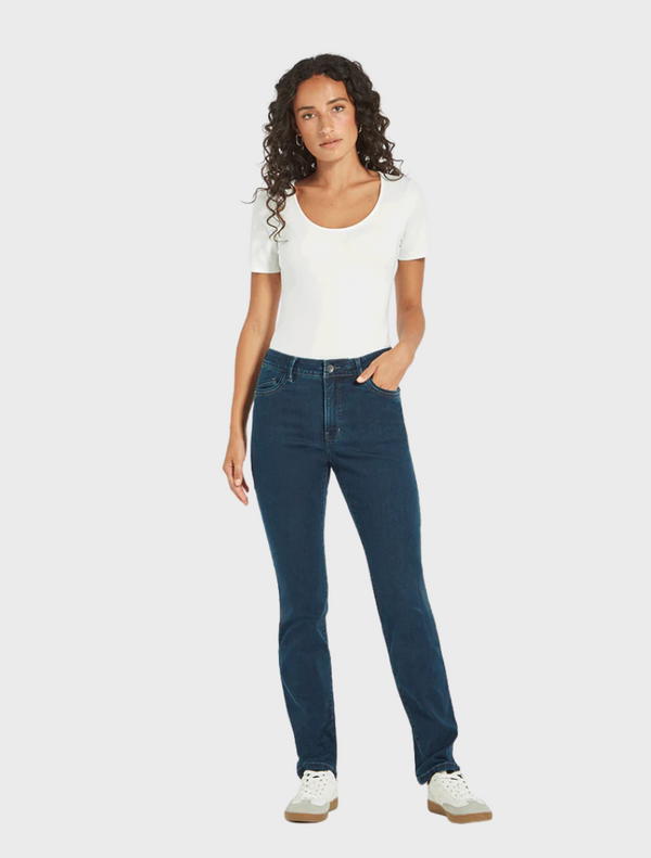 A model dressed in a white shirt and blue jeans stands confidently, showcasing a casual yet stylish outfit.