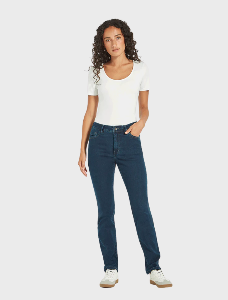 A model dressed in a white shirt and blue jeans stands confidently, showcasing a casual yet stylish outfit.