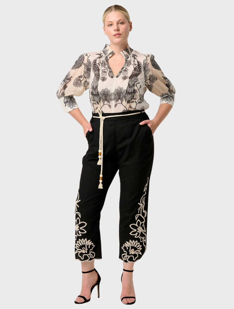 A woman wearing a floral blouse and black skirt, displaying the Oleander Placement Print Cotton Silk design elegantly.