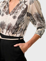 A woman in a floral blouse with a shirred collar and black skirt, featuring the Oleander Placement Print design.