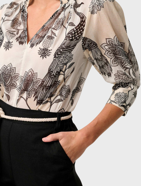 A woman in a floral blouse with a shirred collar and black skirt, featuring the Oleander Placement Print design.