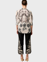 A woman dressed in a floral blouse and black skirt, highlighting the Oleander Placement Print Cotton Silk style.