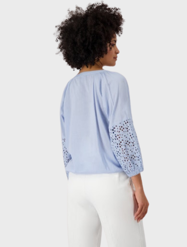A blue blouse with lace sleeves styled with white pants, featuring a delicate openwork design.