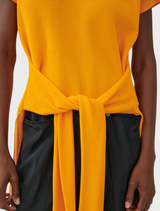 An orange top hanging against a neutral background, highlighting its clean lines and elegant appearance.