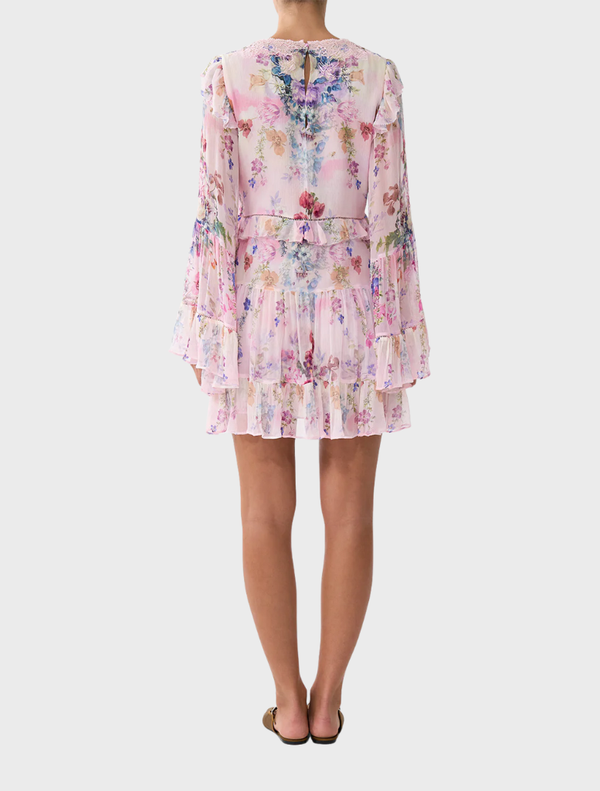 Back view of a woman in a floral print Tiered Swing Mini Dress by Palapast showcasing the dress's vibrant design.