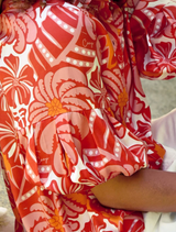 A woman with curly hair, wearing a red and white shirt, stands against a neutral background.
