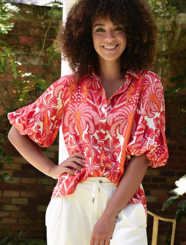 A woman with curly hair wearing a red and white shirt smiles at the camera.