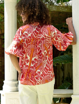 A woman with curly hair, wearing a red and white shirt, stands against a neutral background.