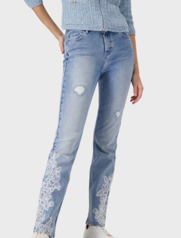 A woman in jeans featuring intricate lace detailing on the pockets and hem, standing confidently with a neutral background.