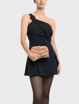 A woman wearing a black dress is holding a multi-patterned Amalia Petite Gathered Clutch purse.