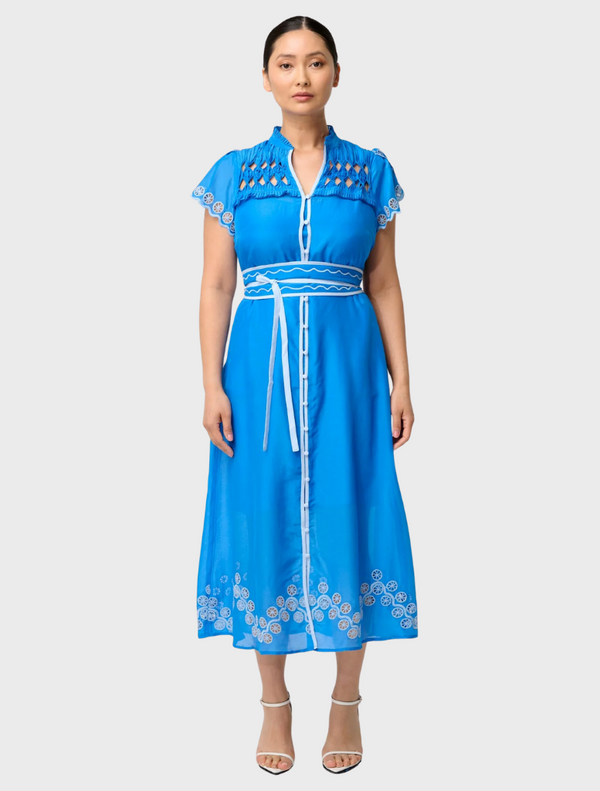  A woman wearing a blue dress with intricate embroidery, showcasing the Petite Xanthia Diamond Smock Yoke design.