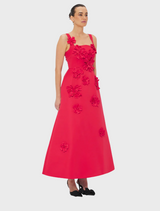  A woman wearing a red dress adorned with floral patterns stands gracefully.