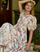 The model is elegantly dressed in a floral-patterned dress, featuring bright blooms on a soft fabric.