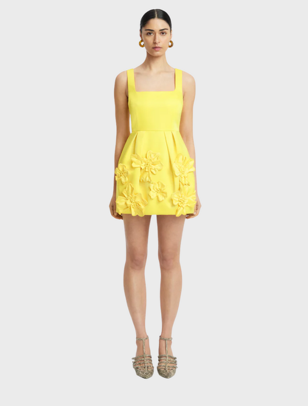 A model poses in a yellow dress adorned with colorful flowers, showcasing a vibrant and cheerful fashion style.